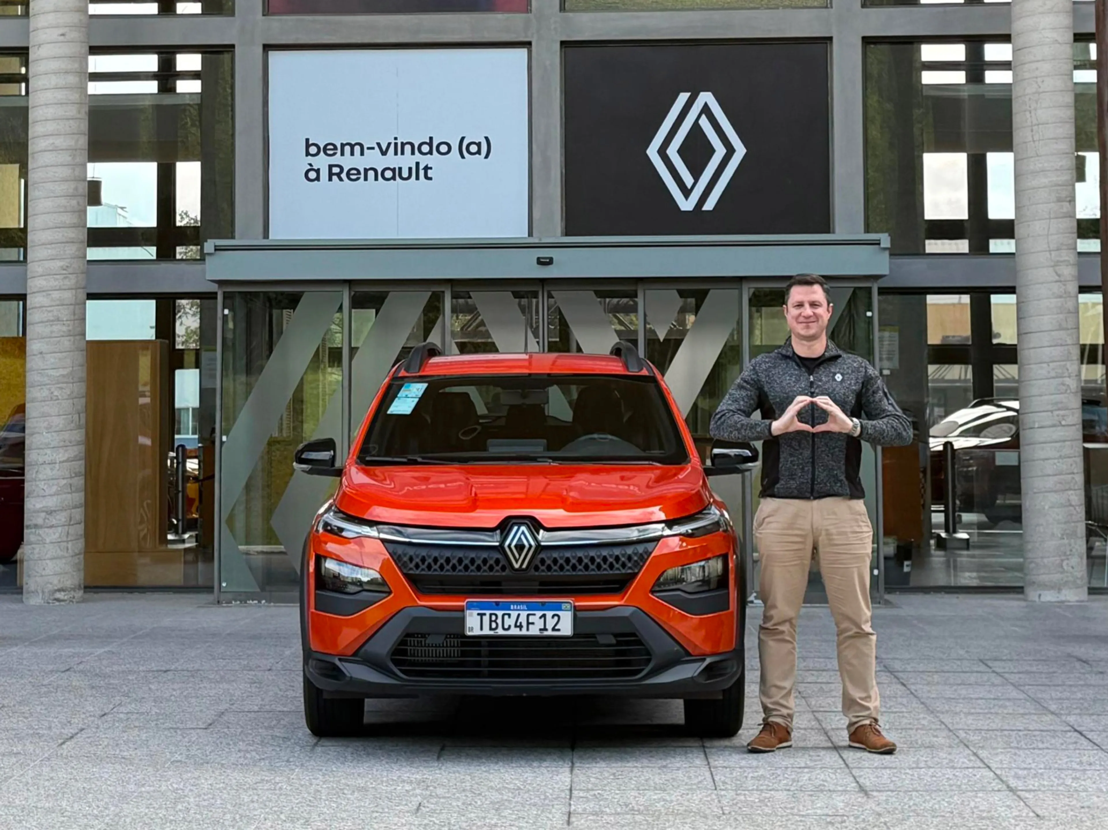 Fabiano à côté d'une Renault faisant le signe de Onehealth avec ses mains
